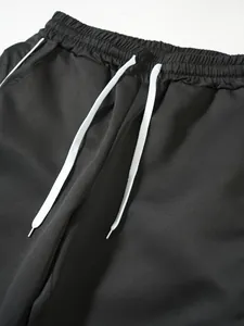 Detailansicht einer schwarzen Herren-Sporthose mit weißem Kordelzug und Gummibund.
