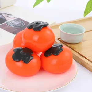 Détail de quatre jouets squishy en forme de kaki orange sur une petite assiette rose