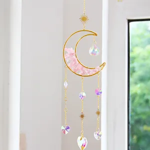 Faceted crystal moon suncatcher with pink crushed stones hanging near a sunny window