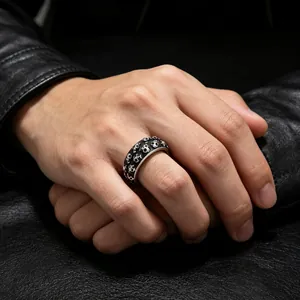 Detailopname van een vintage punk schedelreliëfring van titaniumstaal aan een mannenhand.