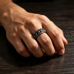 Detail van een vintage ring van titaniumstaal met reliëf schedelpatronen op een hand.