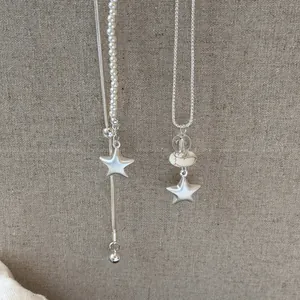 Primer plano de elegantes colgantes de estrella plateados en collares de perlas y mármol