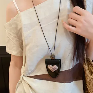 Detail eines Brillenhalter-Anhängers aus Leder mit Herz auf einem hellen Outfit.