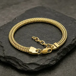 Gros plan d'un bracelet gourmette en acier inoxydable doré sur une ardoise foncée