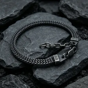 Gros plan d'un bracelet gourmette foxtail robuste présenté sur des roches noires brutes.