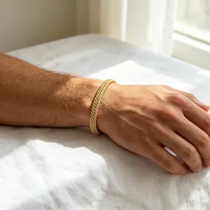 Gros plan d'un bracelet gourmette en or sur un poignet posé sur un fond de lin blanc