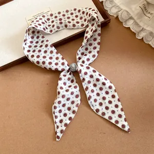Detalle de una bufanda de seda estrecha con estampado floral francés y una perla decorada