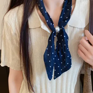 Detalle de un pañuelo de seda azul marino con lunares y un elegante accesorio de perla