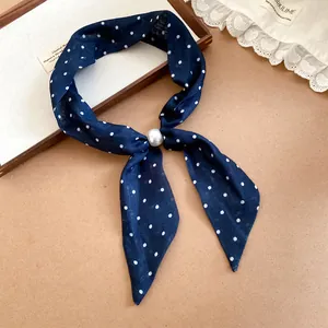 Detalle de un pañuelo azul marino con lunares y una gran perla blanca de adorno.