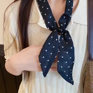 Detalle de una corbata de seda sintética con lunares negros y un anillo decorativo