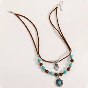 Dettaglio di una collana bohémien a strati con perline turchesi e ciondolo sole.