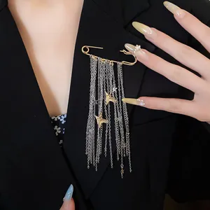 Detail view of a long tassel safety pin brooch with star and bird charms on a black blazer.