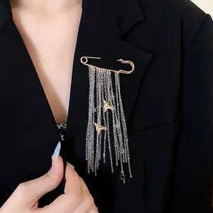 Close-up detail of a gold safety pin brooch with silver tassels and star charms on a black lapel.