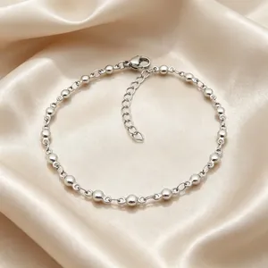 Dettaglio macro di un bracciale minimalista a sfere in acciaio inox argento su tessuto di raso