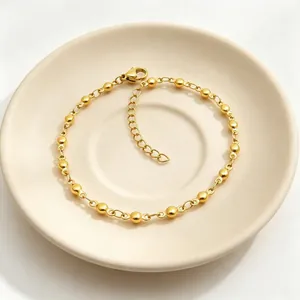 Dettaglio di un bracciale a sfere in acciaio inossidabile dorato su un piatto crema.