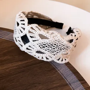 Detail view of a vintage white lace wide headband with black mesh lining on wood.
