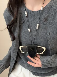 Detail einer Leder-Sonnenbrillenhalter-Halskette mit weißen Perlen auf grauem Cardigan.