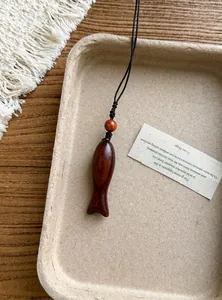Dettaglio macro di un ciondolo a forma di pesce in legno su un vassoio rustico.