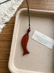 Dettaglio di una collana con ciondolo a forma di pesce in legno su un vassoio ecologico