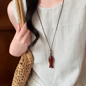 Dettaglio di una collana con ciondolo a forma di pesce in legno su top in lino.