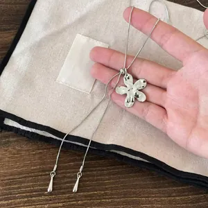 Gros plan d'un collier pendentif fleur argenté avec finition martelée tenu à la main