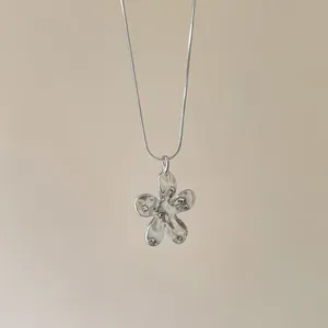 Gros plan détaillé d'un collier pendentif fleur argenté minimaliste sur une chaîne serpent élégante.