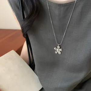 Détail rapproché d'un collier avec pendentif fleur en argent sur un haut en lin