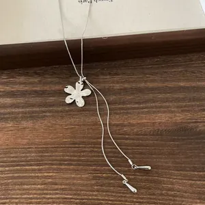 Gros plan d'un collier avec pendentif fleur en argent sur une surface en bois foncé.