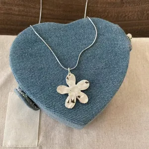 Vue détaillée d'un collier pendentif fleur argenté minimaliste sur un cœur en denim bleu