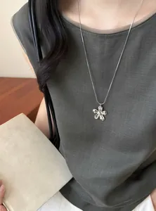 Gros plan d'un collier avec pendentif fleur argenté minimaliste sur un mannequin chic.