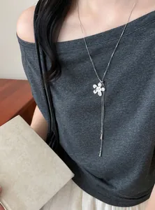 Détail d'un collier pendentif fleur en argent porté sur un haut gris élégant