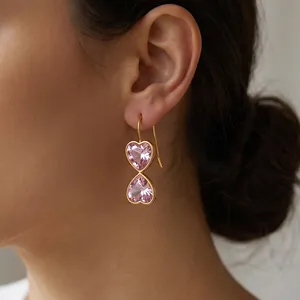 Close-up view of elegant gold heart earrings with pink rhinestones on a female model's ear