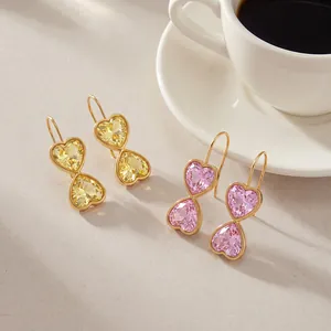 Detail of elegant gold-plated heart-shaped crystal drop earrings in yellow and pink colors.