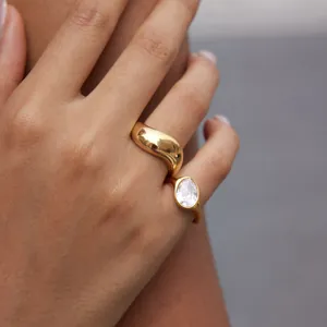 Close-up detail shot of a gold wavy dome ring and a teardrop zircon ring on a hand