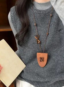 Detailansicht einer modischen Halskette mit Lederbär-Anhänger auf einer grauen Strickweste