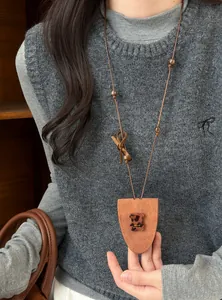 Nahaufnahme einer modischen braunen Leder-Bär-Halskette auf einem grauen Strickpullunder.