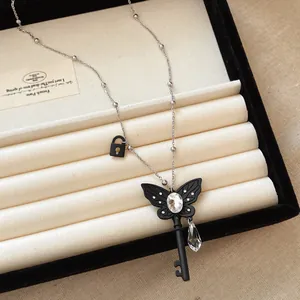 Detail of butterfly key pendant necklace with teardrop crystal and black lock charm.