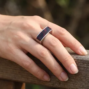 Gros plan d'une bague vintage carrée en acier inoxydable avec résine rouge sur une main.