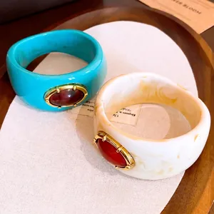 Brazalete ancho de resina marbreada con detalle de gema ovalada.