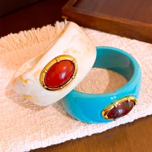 Primer plano detallado de brazaletes de resina anchos con textura jaspeada y piedras ovales
