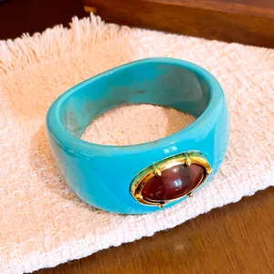 Primer plano de un brazalete ancho de resina turquesa con una piedra roja ovalada