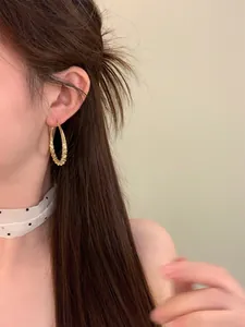 Eleganter goldener Tropfen-Creolen-Ohrring mit Textur am Model für Mode-Look.