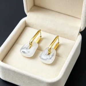 Macro detail of geometric gold-plated earrings with white marble resin in a jewelry box