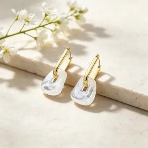 Macro detail view of minimalist geometric gold hoops with marbled white resin pendants