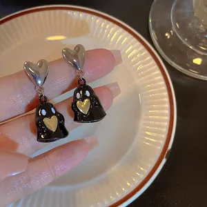 Detail view of cute black ghost earrings with silver heart studs and gold heart charms.