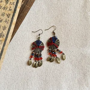 Close-up of vintage ethnic earrings with woven thread, crystals, and bronze leaf charms.