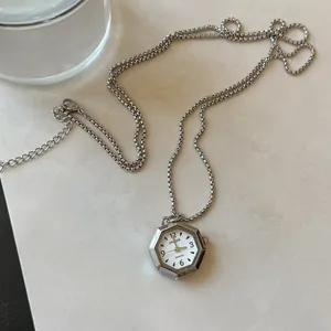 Vintage style hexagonal watch pendant necklace with silver chain on marble surface