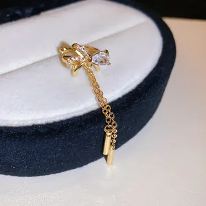 Detailed view of a gold-tone bow ear cuff featuring sparkling zircon stones and long chain tassels.
