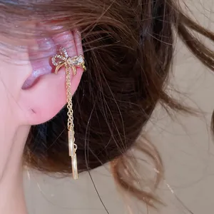 Detailed macro view of a zircon bow ear cuff with elegant long gold tassel pendants