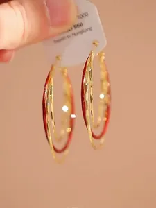 Detailopname van elegante meerlaagse rode en goudkleurige metalen oorringen